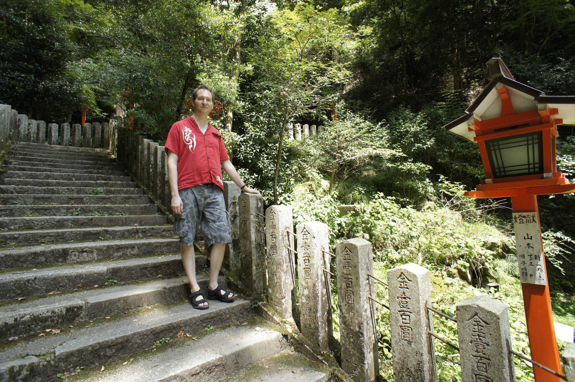 Dr. Mark Hosak in rotem Hemd auf der Steintreppe am Kurama-Tempel bei Kyōto, neben einer roten Holzlaterne