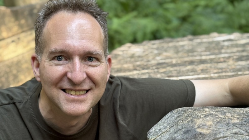 Dr. Mark Hosak in the forest with a wooden eagle
